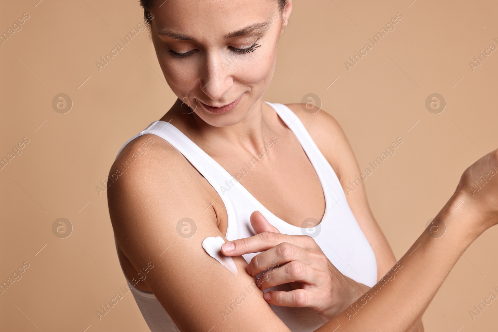 Photo of Beautiful woman applying cream onto arm against beige background. Body care