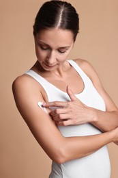 Photo of Beautiful woman applying cream onto arm against beige background. Body care