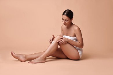 Photo of Beautiful woman applying cream onto leg against beige background. Body care