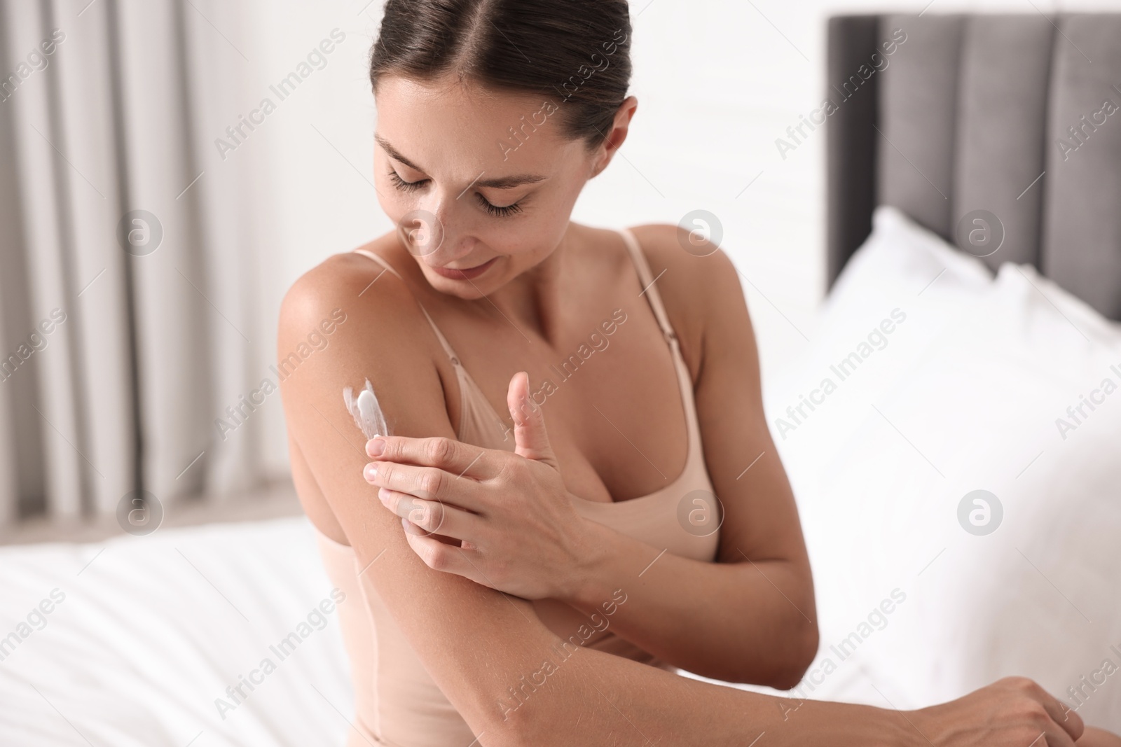 Photo of Beautiful woman with perfect skin applying cream onto shoulder on bed. Body care