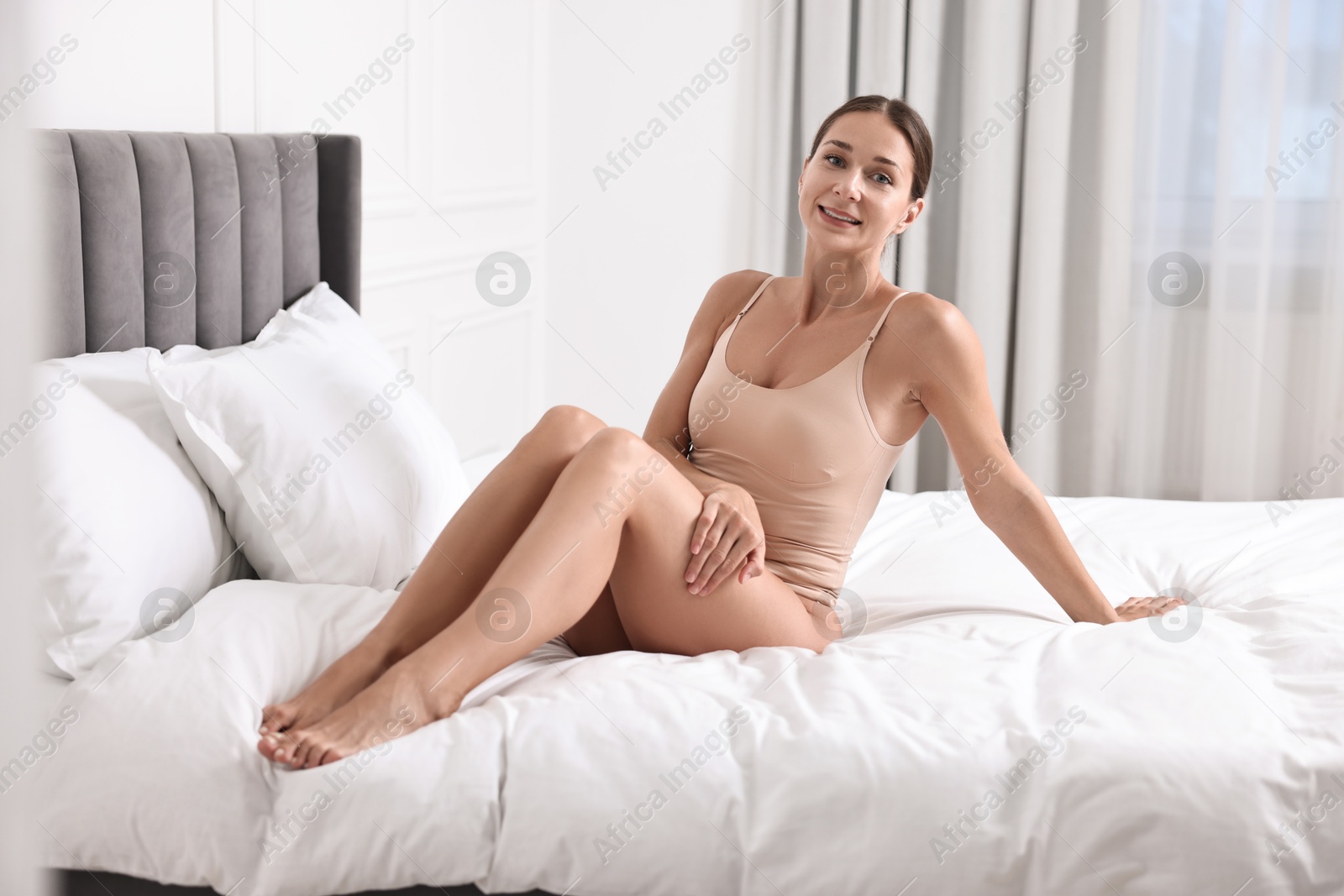 Photo of Smiling woman with perfect skin posing on bed. Body care