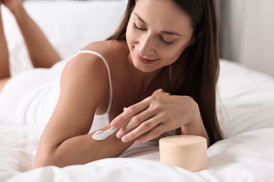 Photo of Beautiful woman with perfect skin applying cream onto hand on bed. Body care