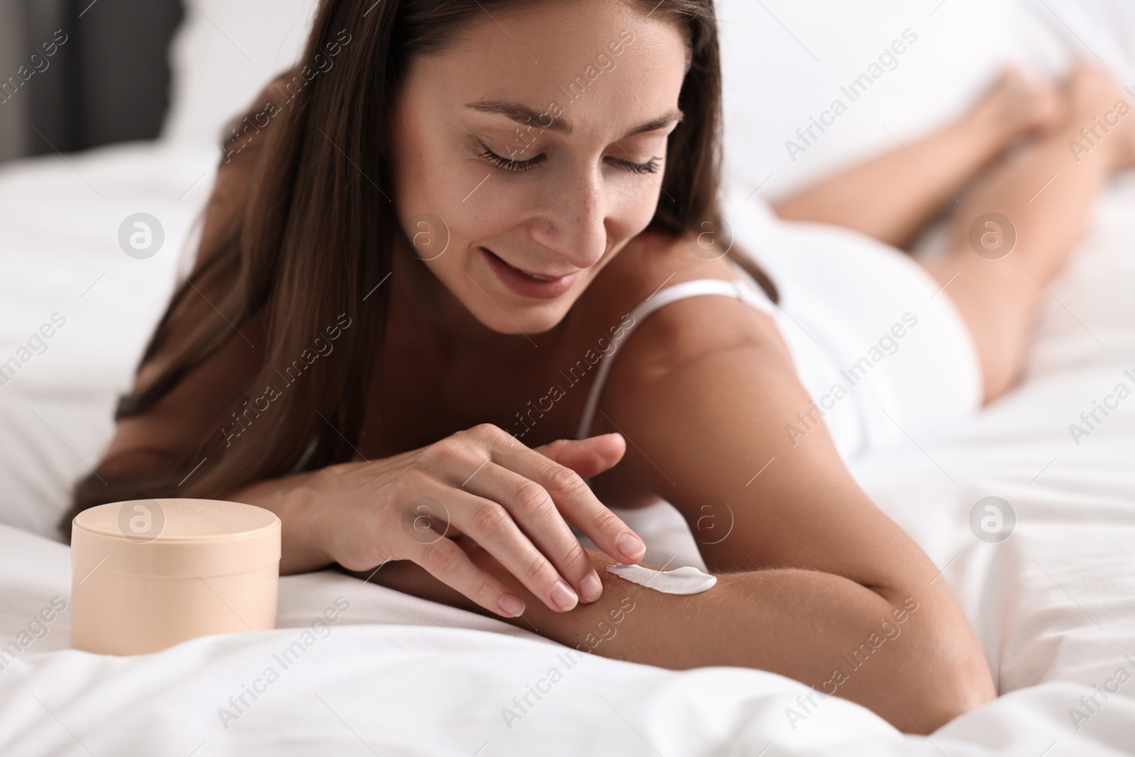 Photo of Beautiful woman with perfect skin applying cream onto hand on bed. Body care