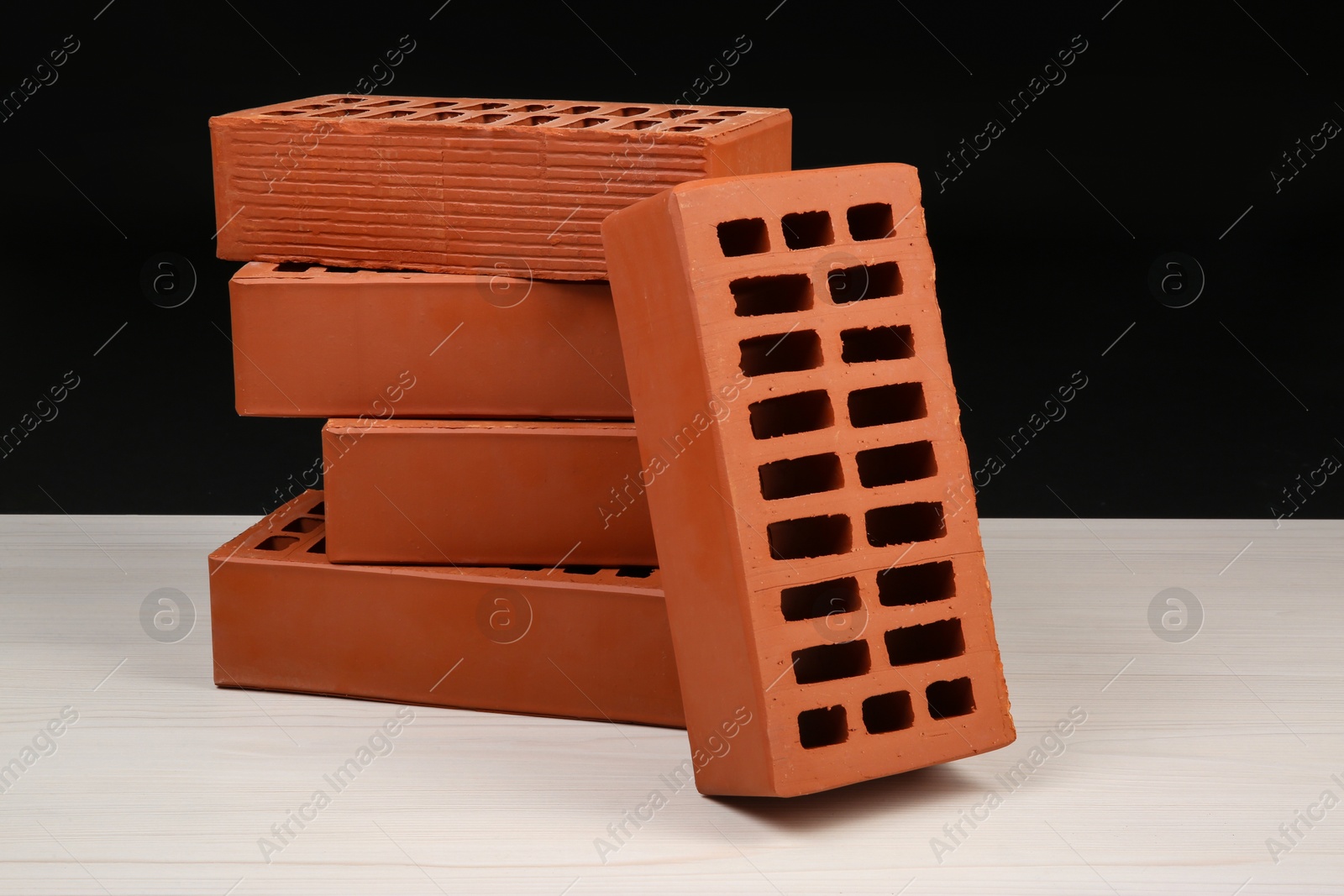 Photo of Many red bricks on light wooden table against black background. Building material