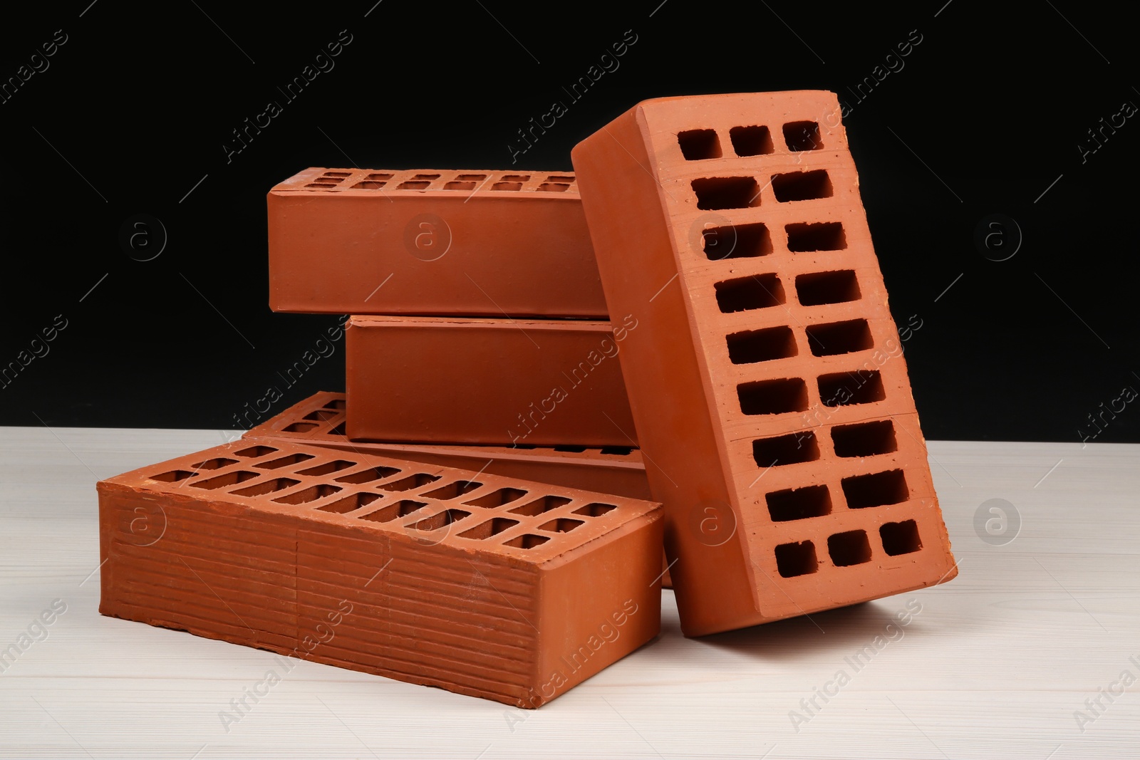 Photo of Many red bricks on light wooden table against black background. Building material