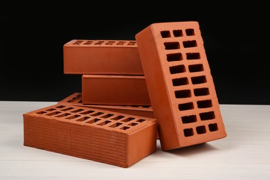 Photo of Many red bricks on light wooden table against black background. Building material