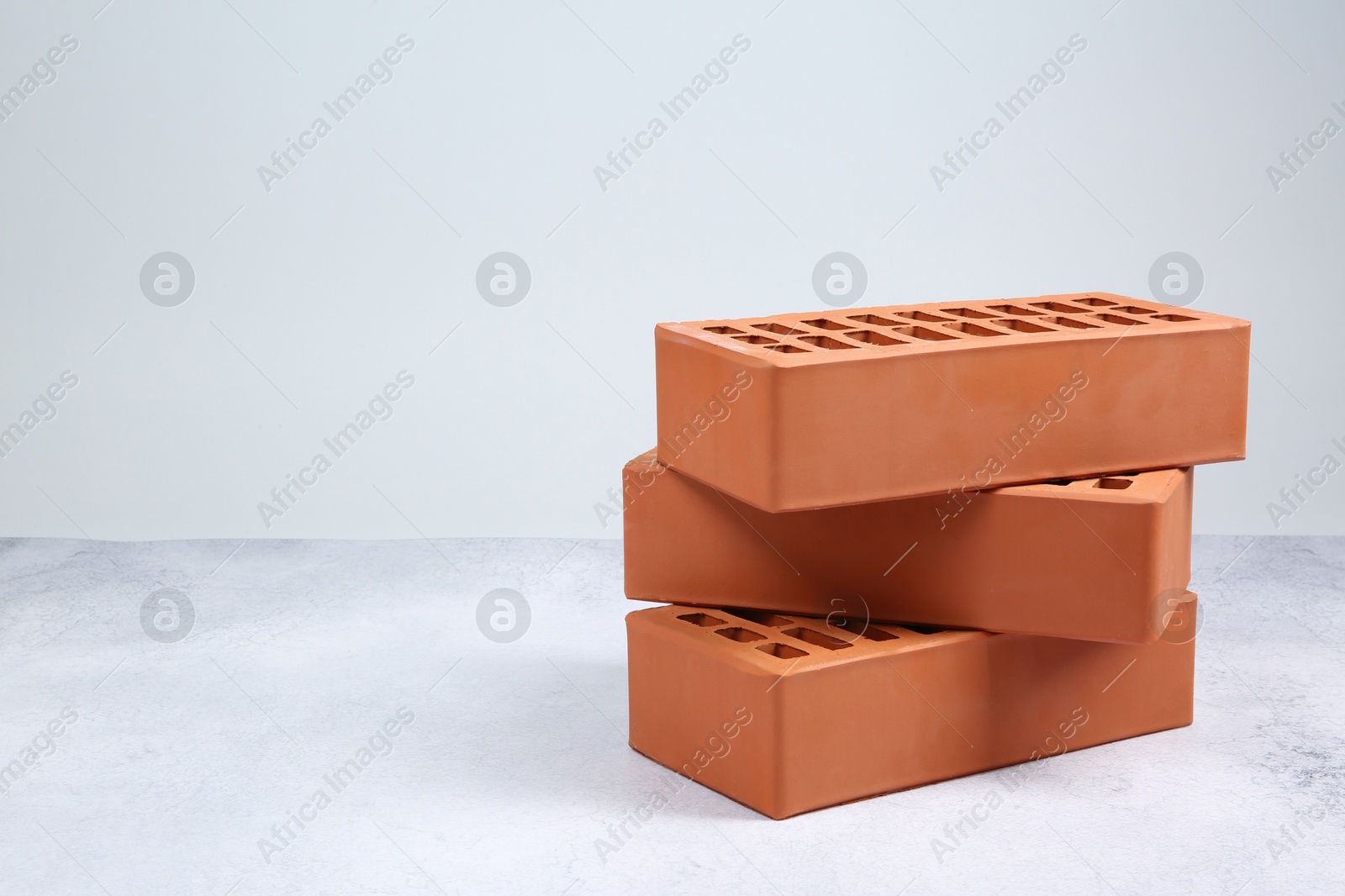 Photo of Three red bricks on textured table against light background, space for text. Building material