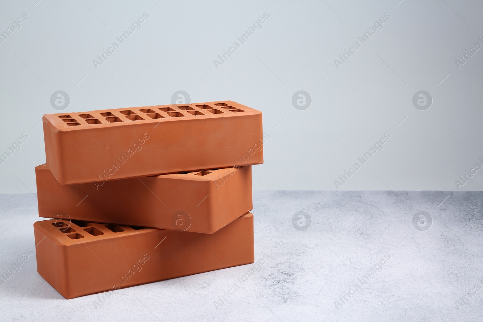 Photo of Three red bricks on textured table against light background, space for text. Building material