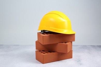 Photo of Stack of red bricks and hard hat on textured table against light background. Building material