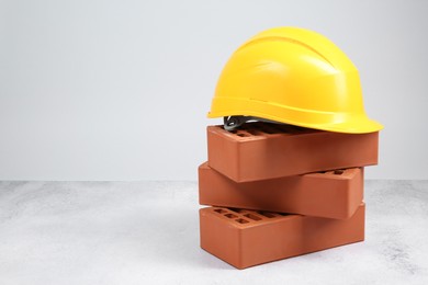 Photo of Stack of red bricks and hard hat on textured table against light background. Space for text