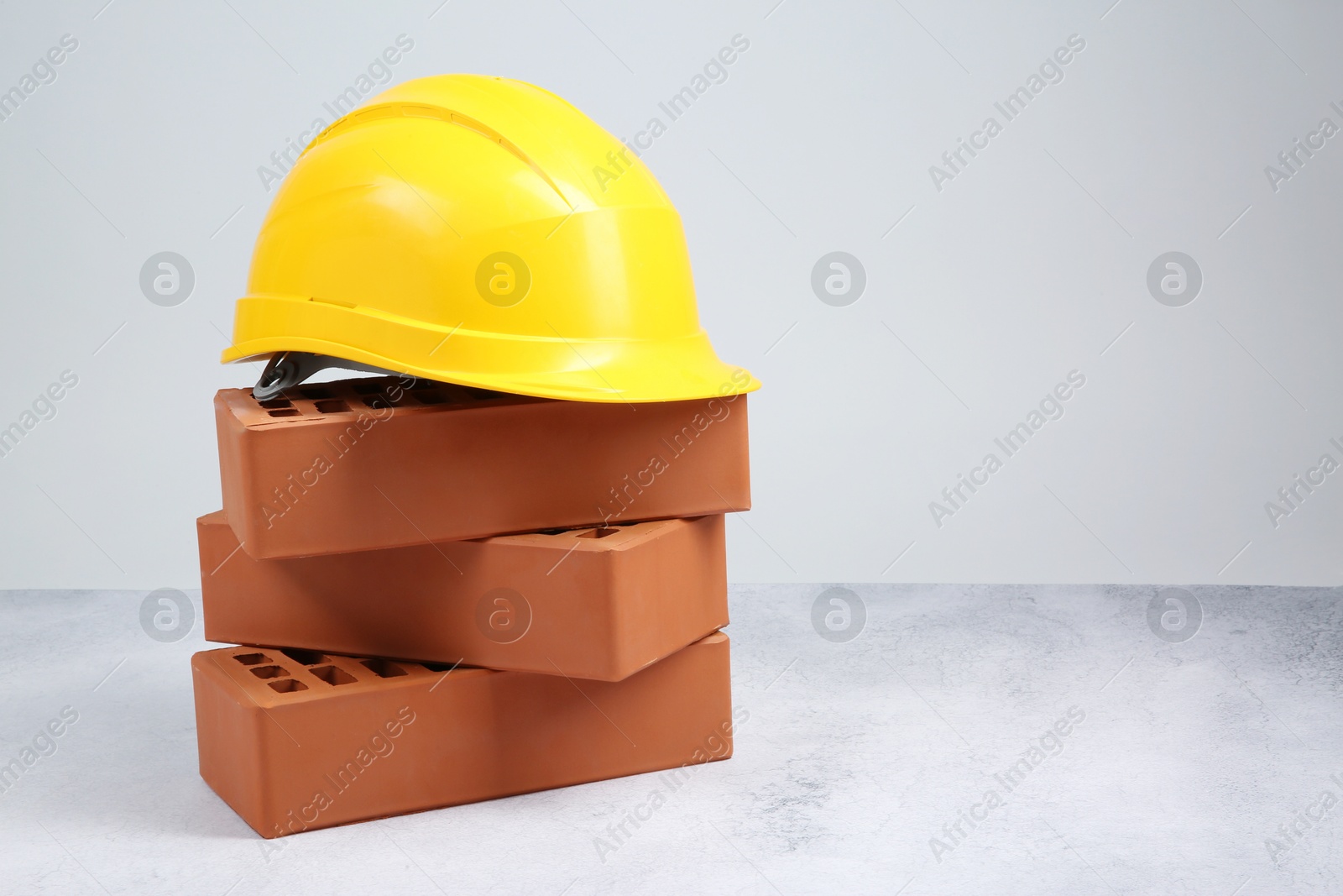 Photo of Stack of red bricks and hard hat on textured table against light background. Space for text