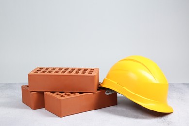 Photo of Red bricks and hard hat on textured table against light background