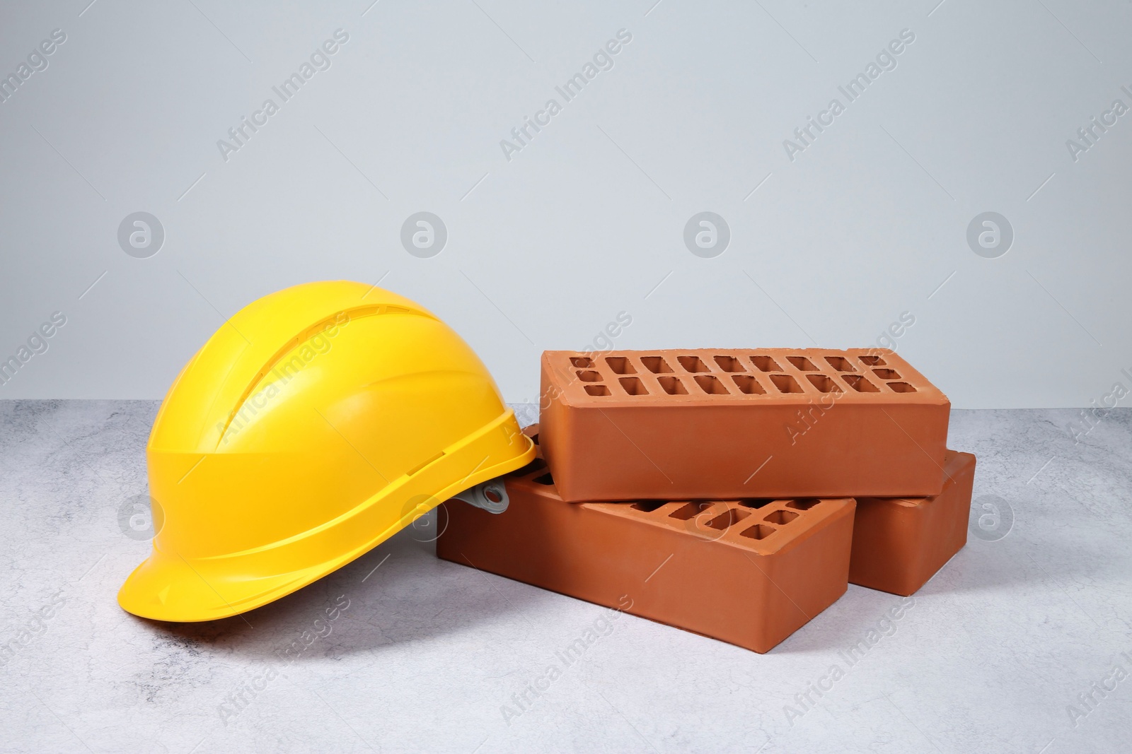 Photo of Red bricks and hard hat on textured table against light background