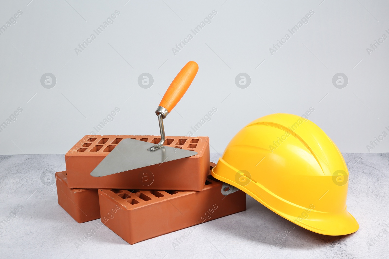 Photo of Red bricks, trowel and hard hat on textured table against light background