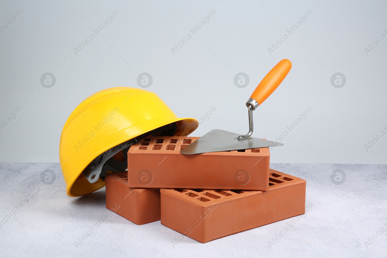 Photo of Red bricks, trowel and hard hat on textured table against light background