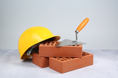 Photo of Red bricks, trowel and hard hat on textured table against light background