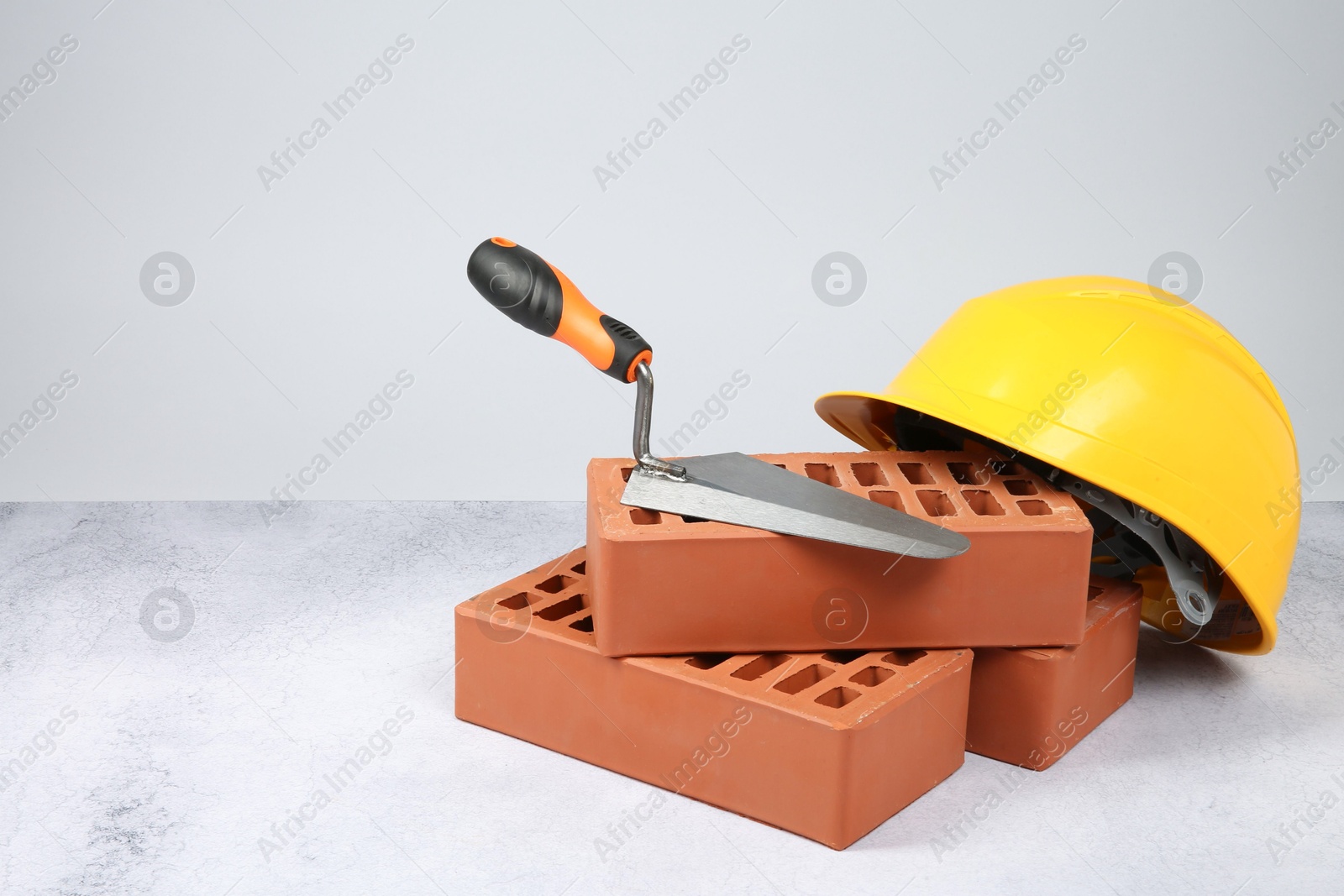 Photo of Red bricks, trowel and hard hat on textured table against light background. Space for text