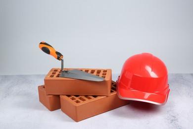 Photo of Red bricks, trowel and hard hat on textured table against light background