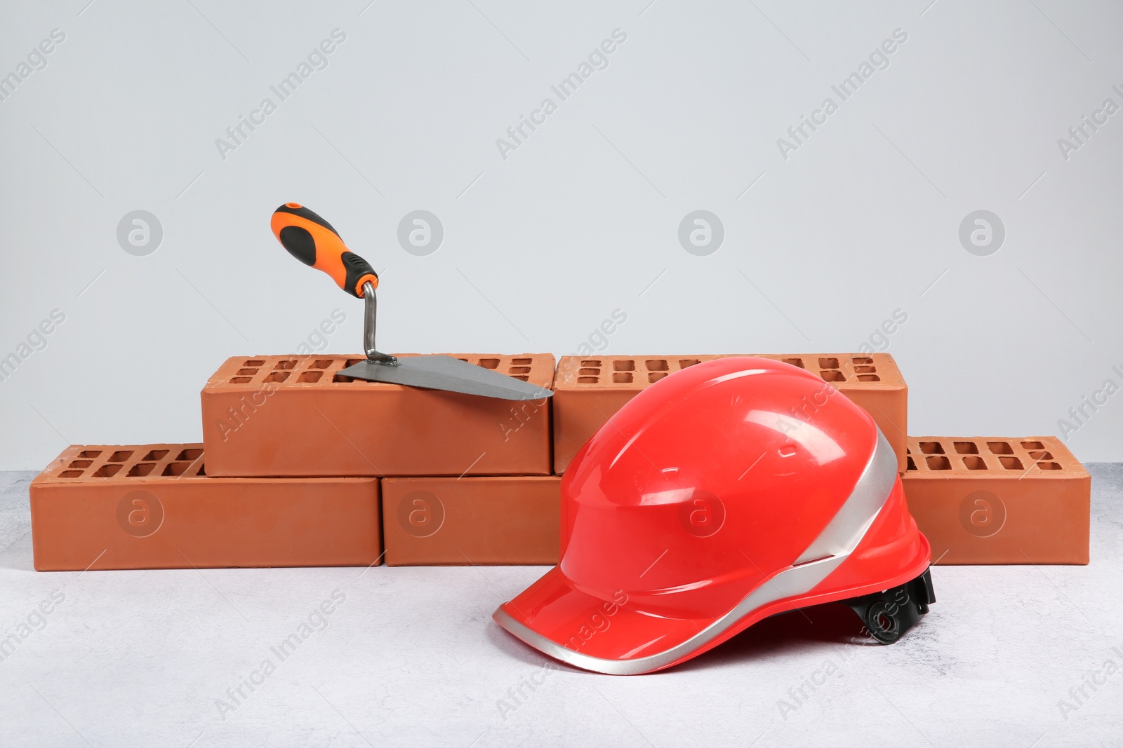 Photo of Red bricks, trowel and hard hat on textured table against light background