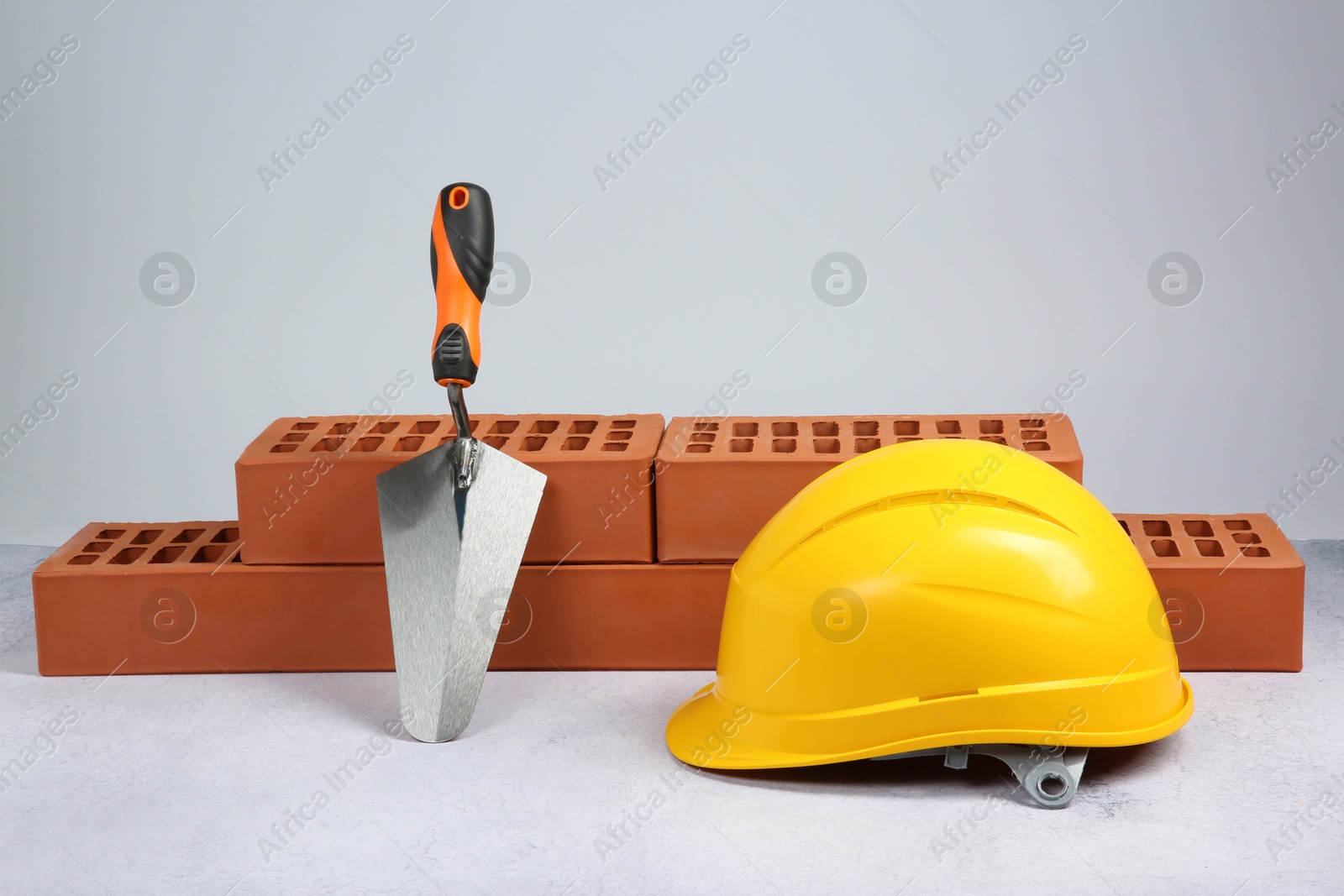 Photo of Red bricks, trowel and hard hat on textured table against light background