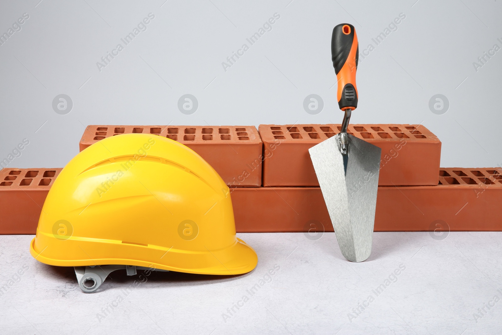 Photo of Red bricks, trowel and hard hat on textured table against light background