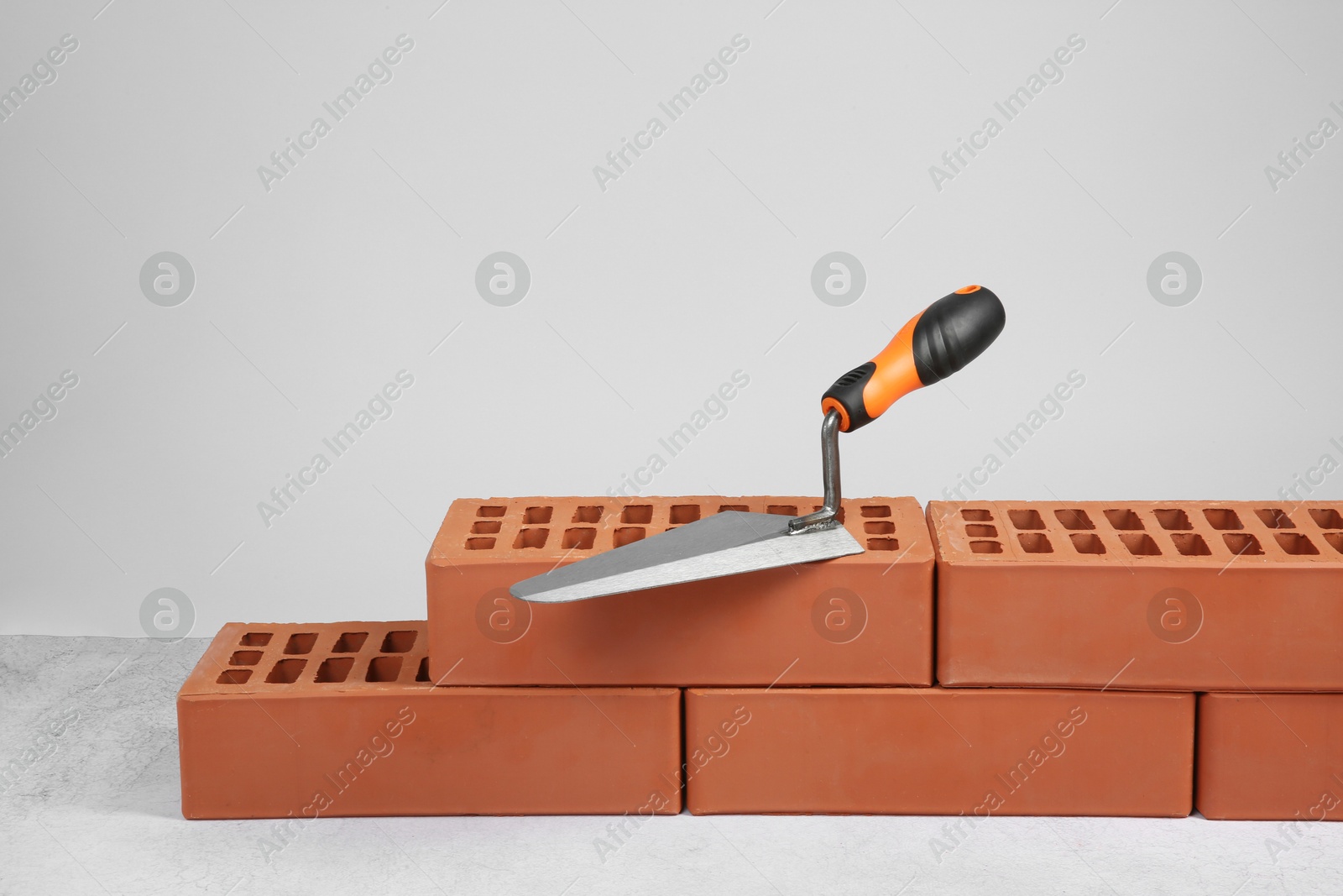 Photo of Red bricks and trowel on textured table against light background. Building material