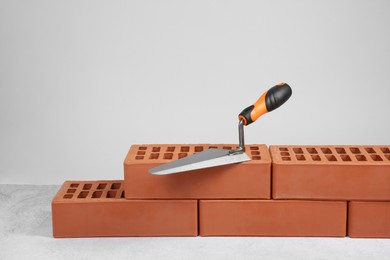 Photo of Red bricks and trowel on textured table against light background. Building material