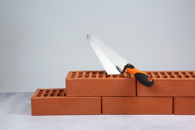 Photo of Red bricks and trowel on textured table against light background. Building material