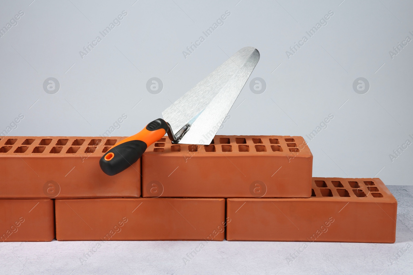 Photo of Red bricks and trowel on textured table against light background. Building material