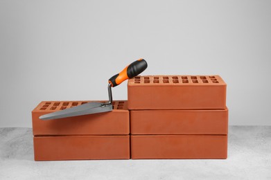 Photo of Red bricks and trowel on textured table against light background. Building material