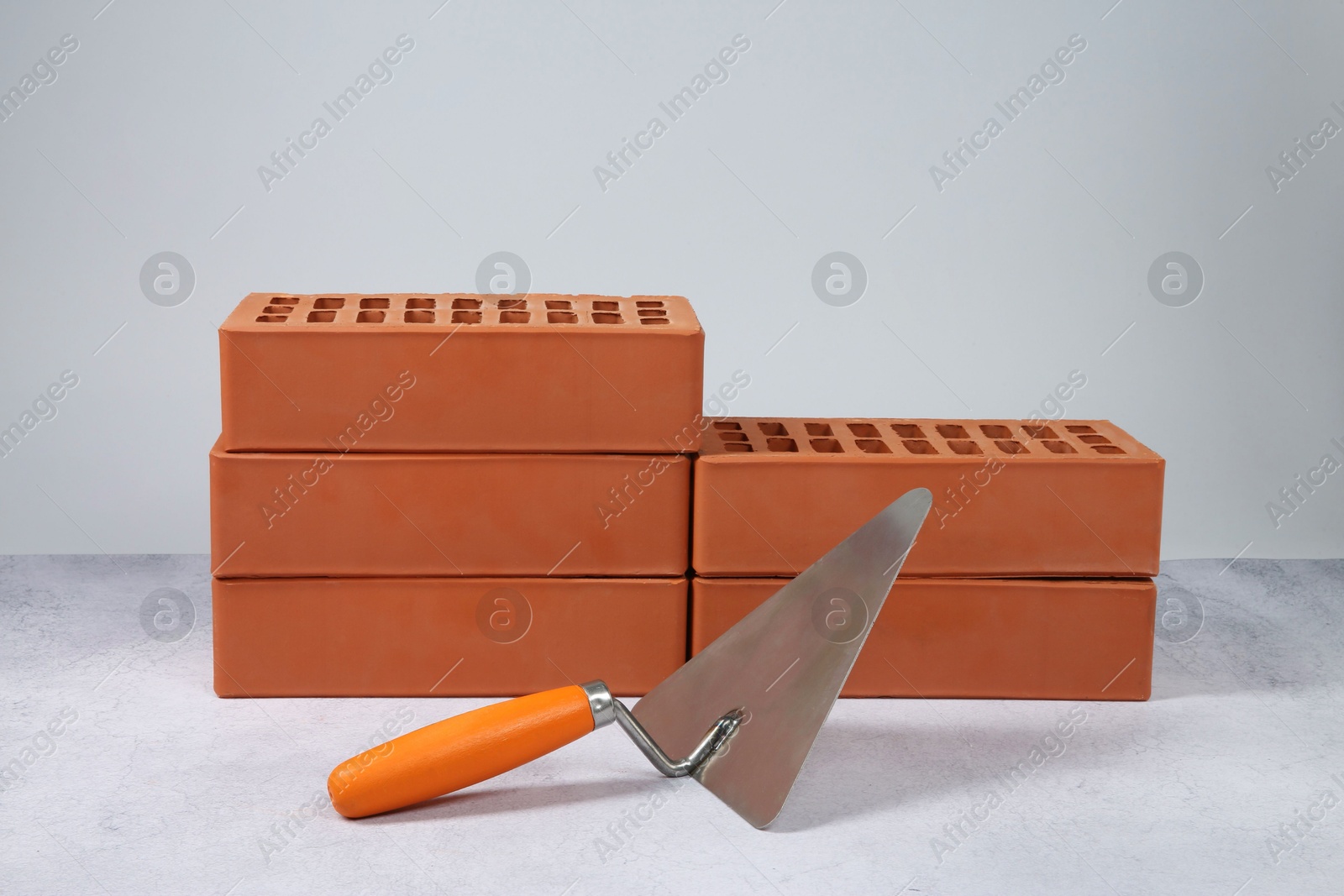 Photo of Red bricks and trowel on textured table against light background. Building material