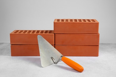 Photo of Red bricks and trowel on textured table against light background. Building material