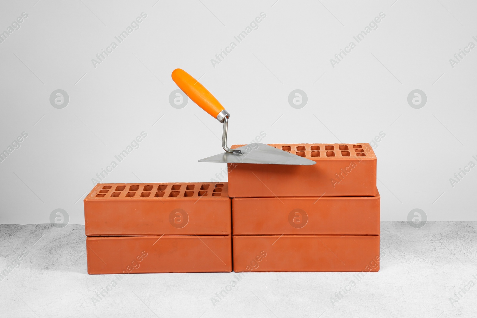 Photo of Red bricks and trowel on textured table against light background. Building material