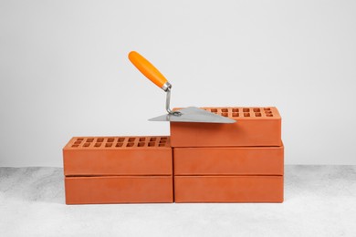 Photo of Red bricks and trowel on textured table against light background. Building material