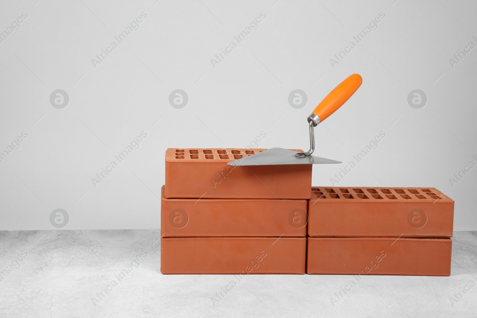 Photo of Red bricks and trowel on textured table against light background. Space for text