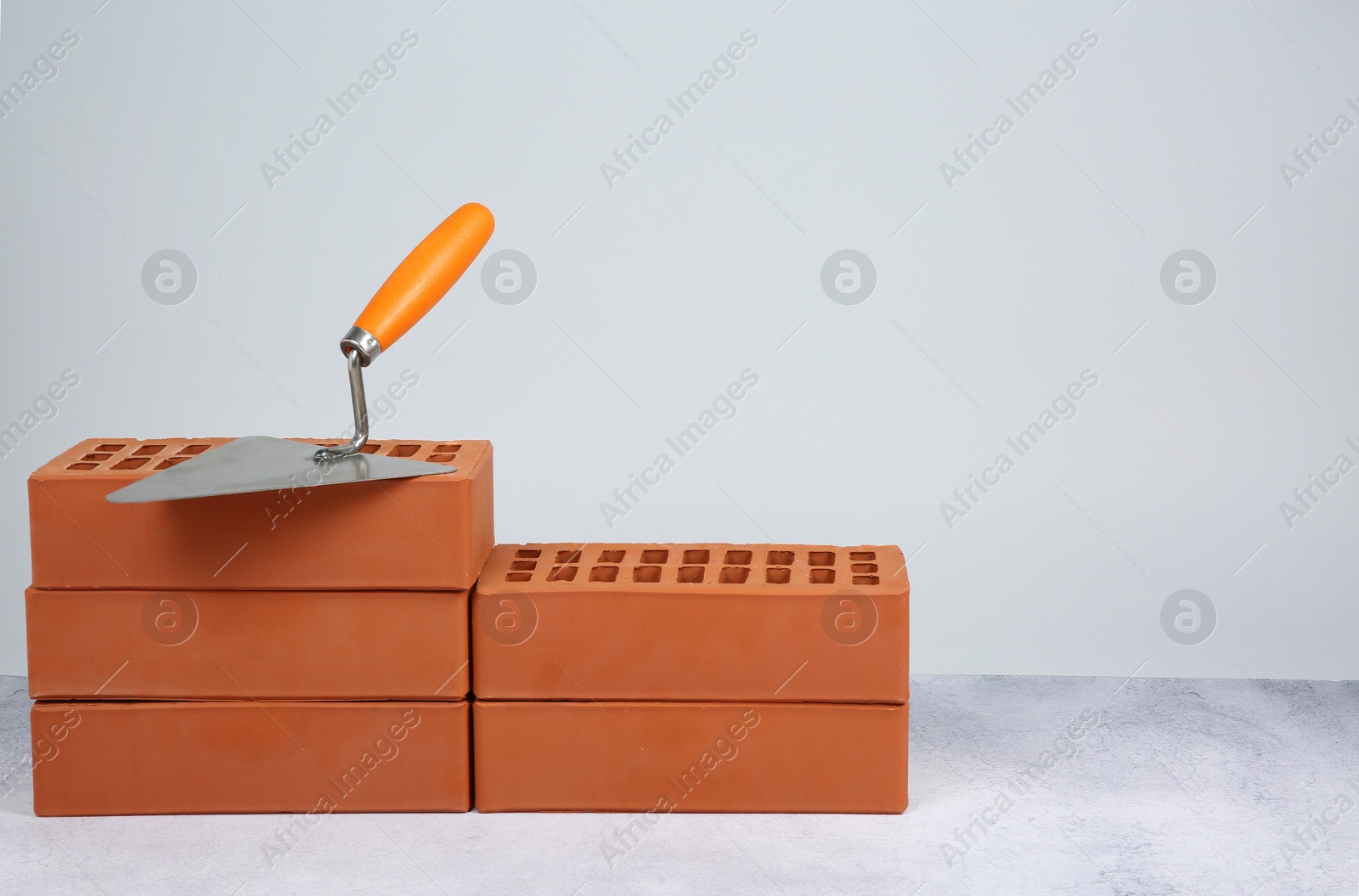 Photo of Red bricks and trowel on textured table against light background. Space for text