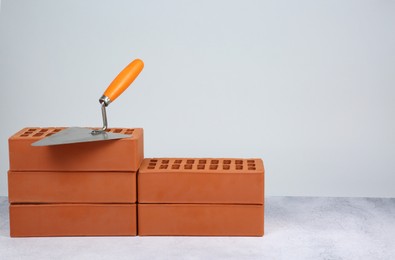 Red bricks and trowel on textured table against light background. Space for text