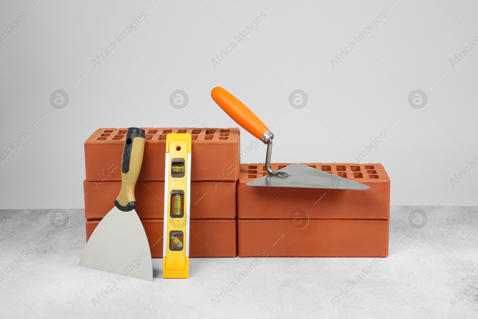 Photo of Red bricks, trowels and building level on textured table against light background