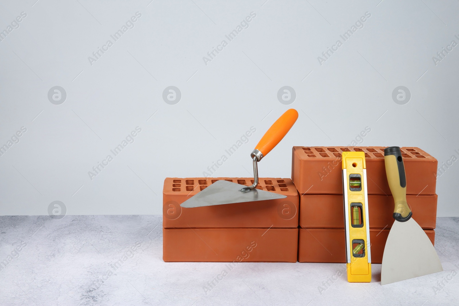 Photo of Red bricks, trowels and building level on textured table against light background. Space for text