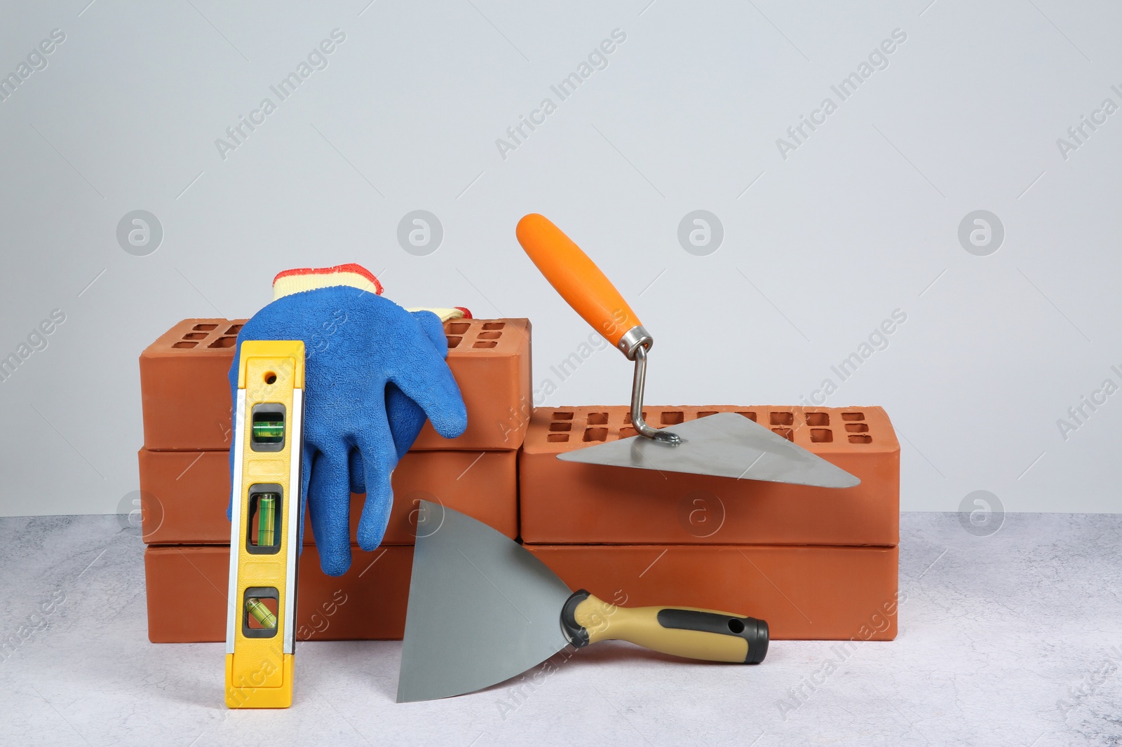 Photo of Red bricks, trowels, gloves and building level on textured table against light background