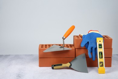 Red bricks, trowels, gloves and building level on textured table against light background. Space for text