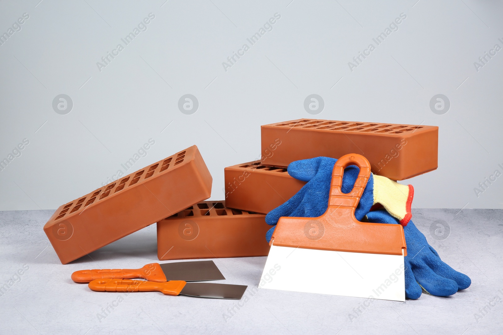 Photo of Red bricks, trowels and gloves on textured table against light background