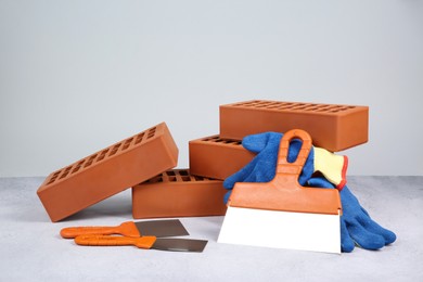 Photo of Red bricks, trowels and gloves on textured table against light background