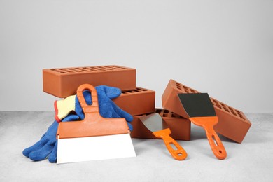 Photo of Red bricks, trowels and gloves on textured table against light background