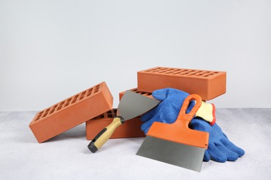 Photo of Red bricks, trowels and gloves on textured table against light background