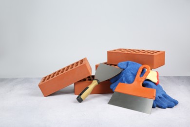 Photo of Red bricks, trowels and gloves on textured table against light background. Space for text