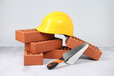 Photo of Red bricks, trowel and hardhat on textured table against light background