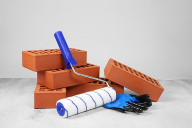 Red bricks, paint roller and gloves on textured table against light background