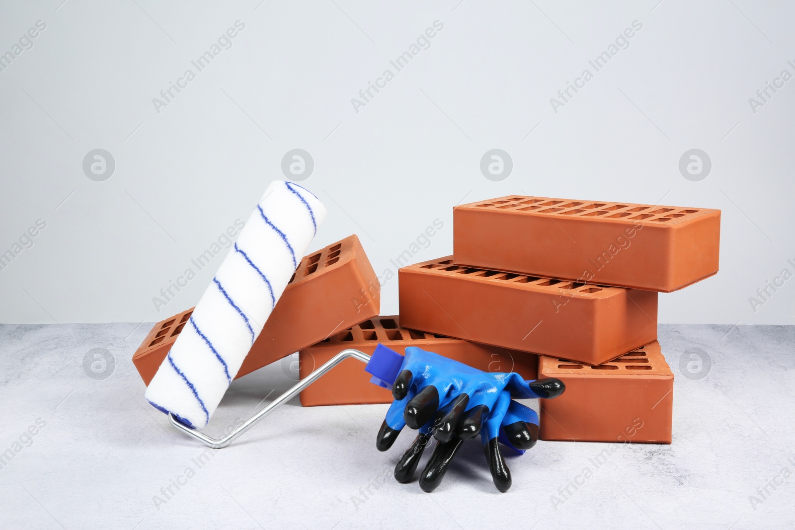 Photo of Red bricks, paint roller and gloves on textured table against light background