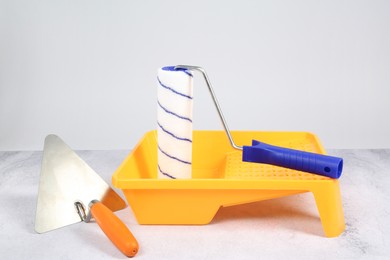 Photo of Paint roller, trowel and yellow tray on textured table against light background. Building material